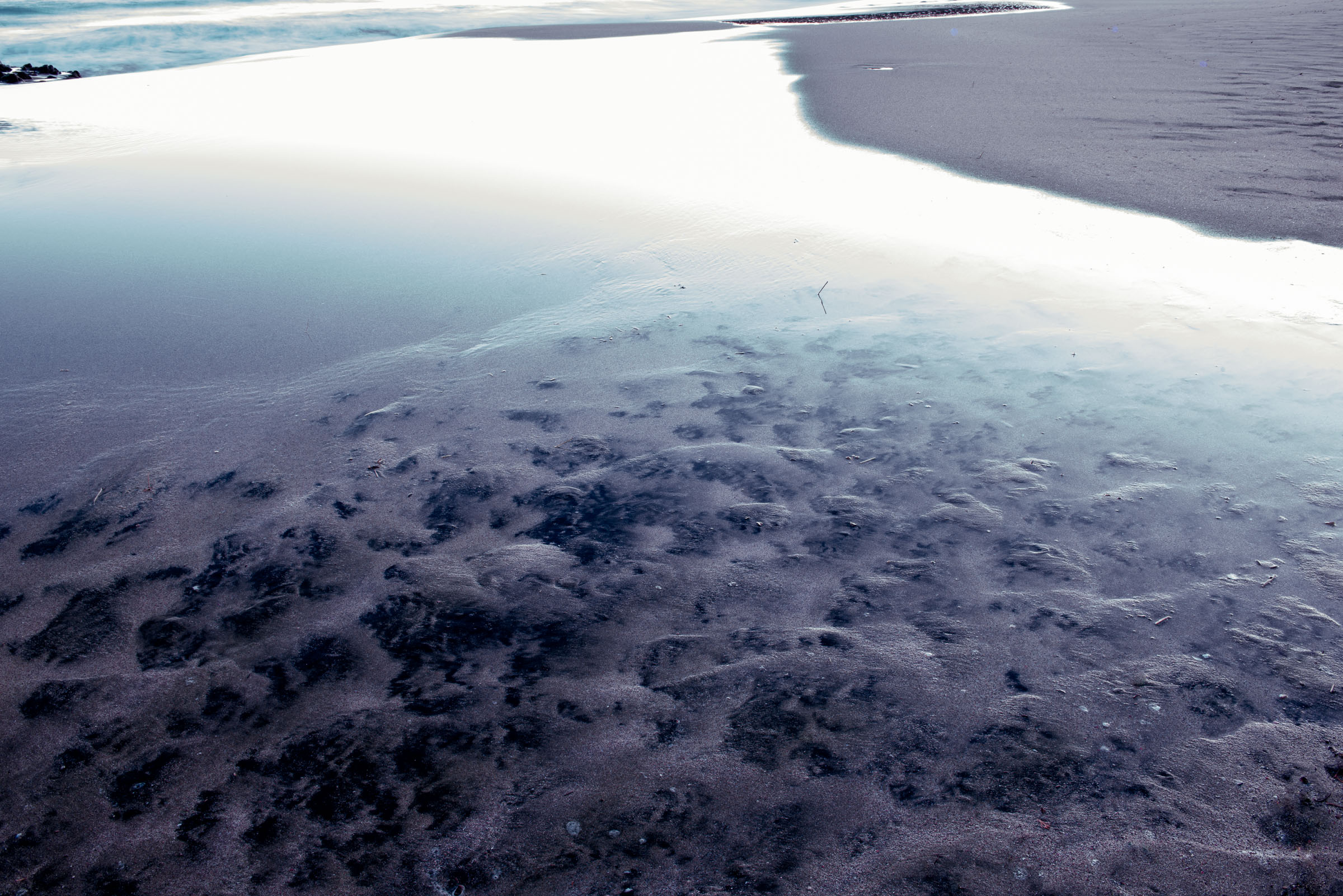 Reflective tidal pool curving through dark sand