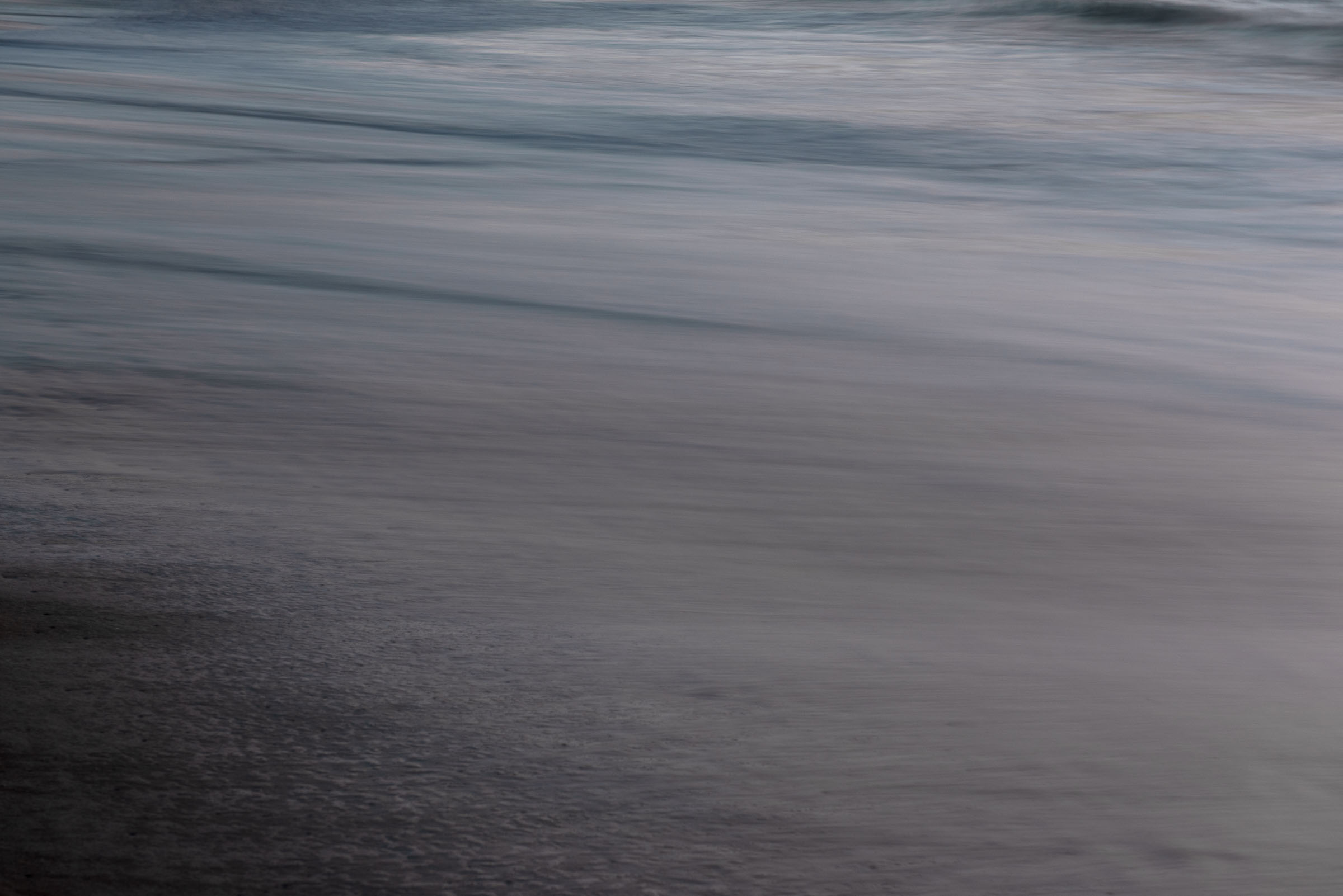 Blurred horizontal bands of grey water and wet sand