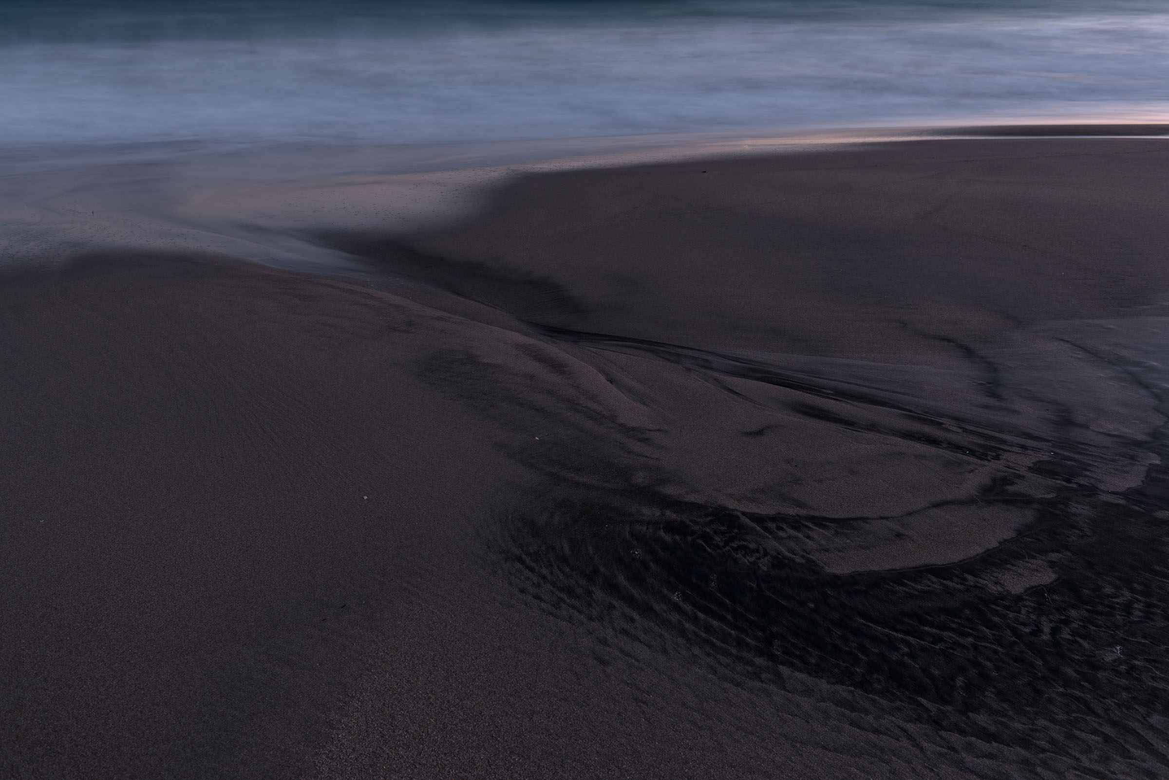 A narrow stream cut through dark sand at the shoreline