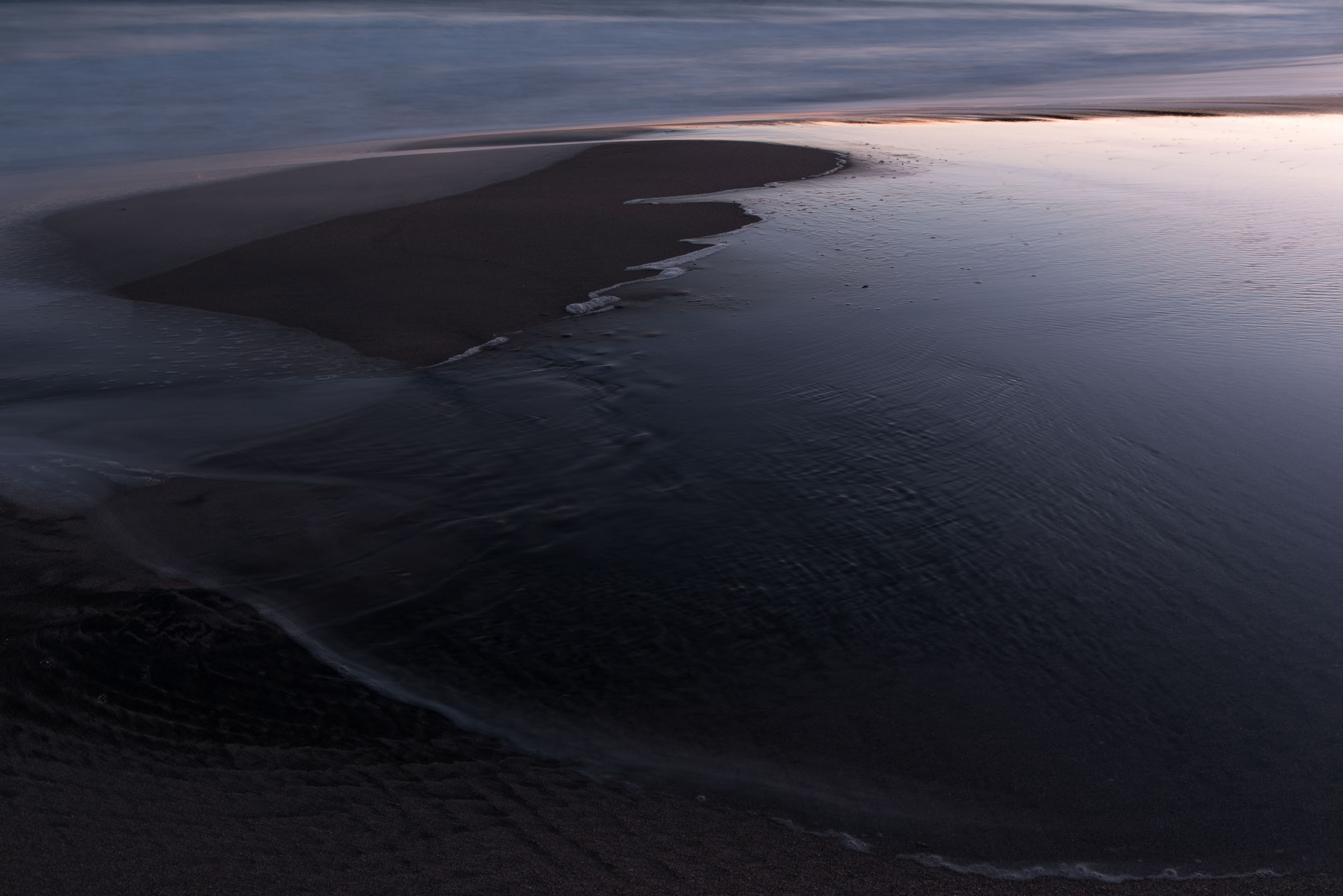 Shallow water surrounding a curved dark sandbar