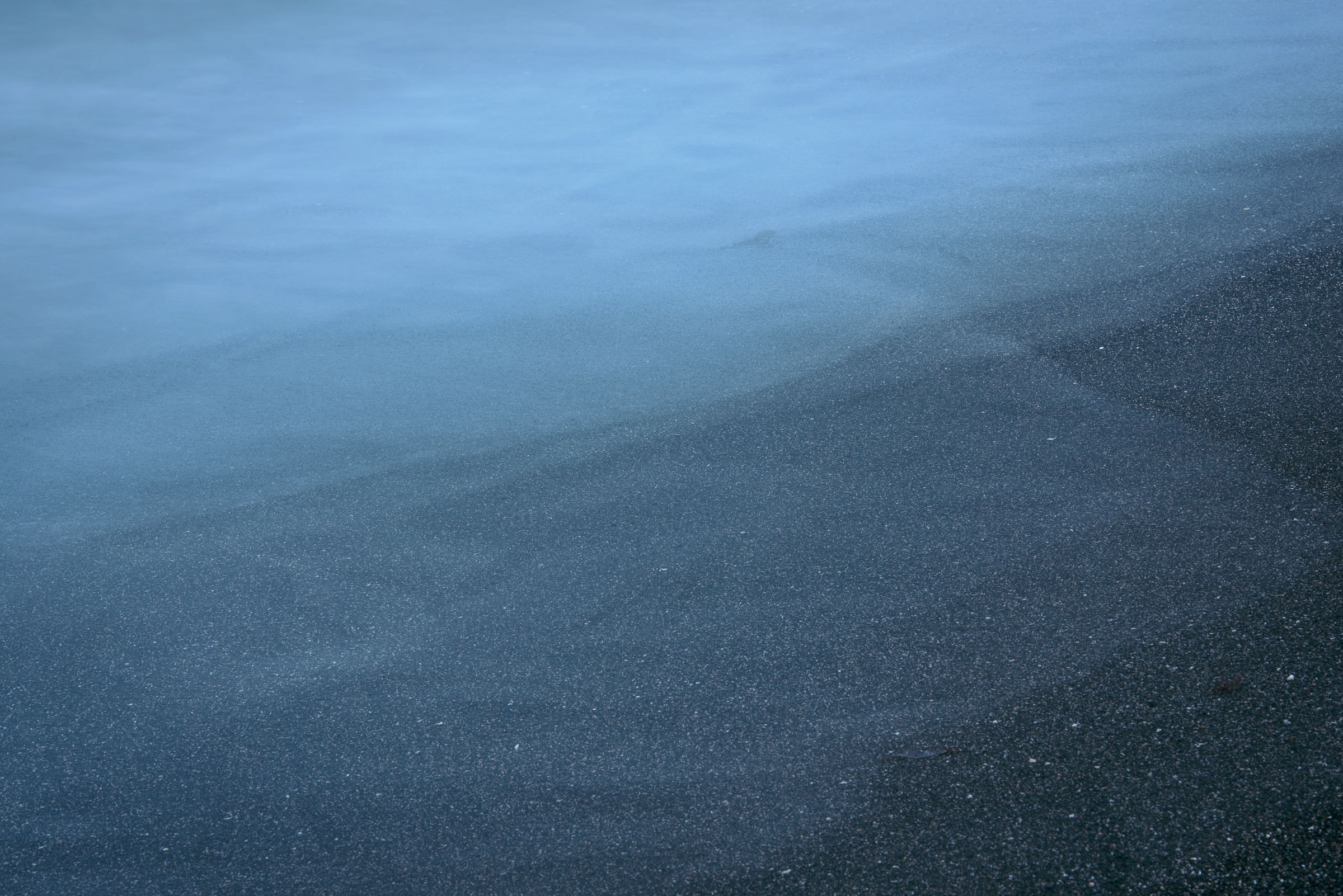 A thin sheet of blue water crossing dark sand
