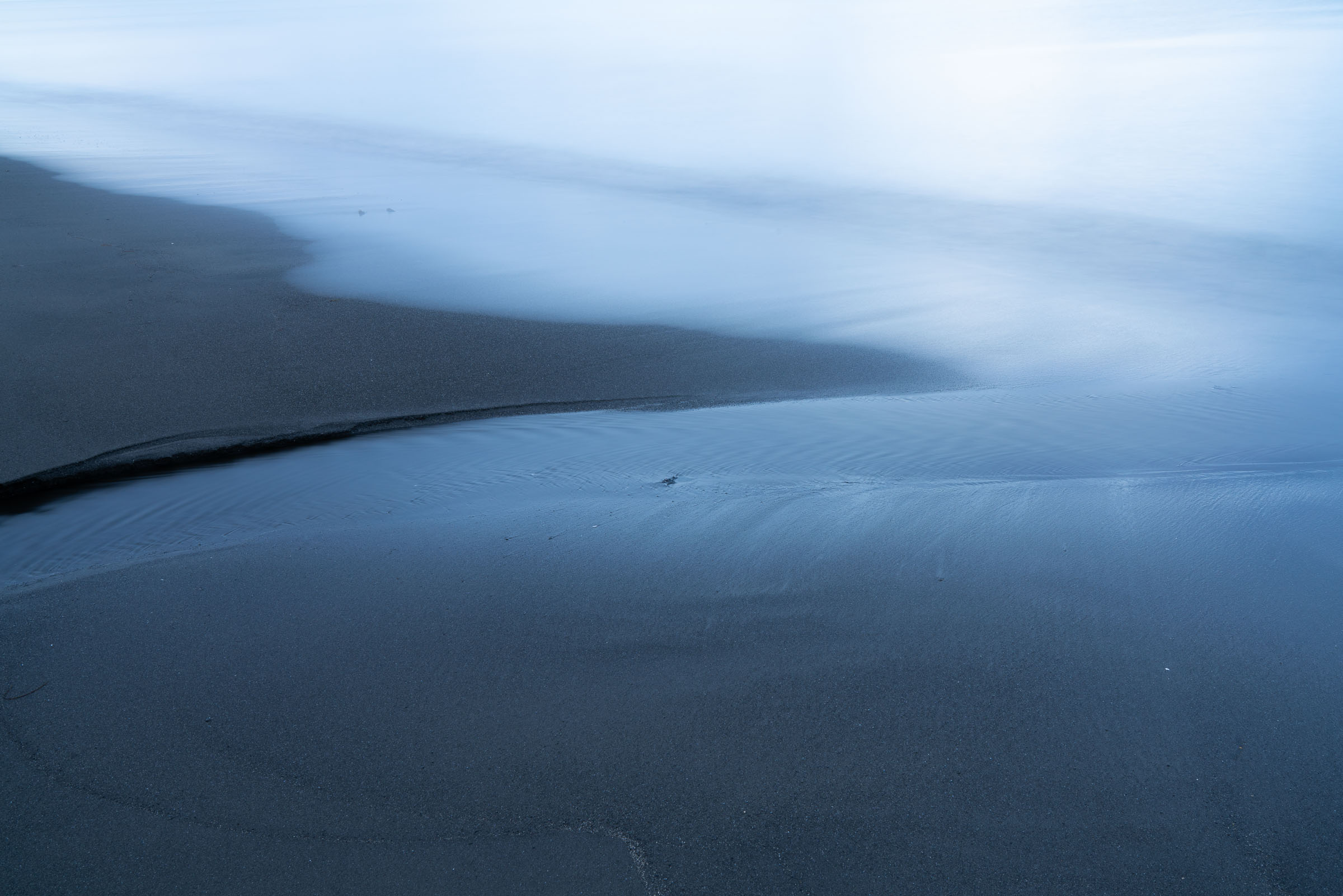 Pale blue water winding between dark sandbanks