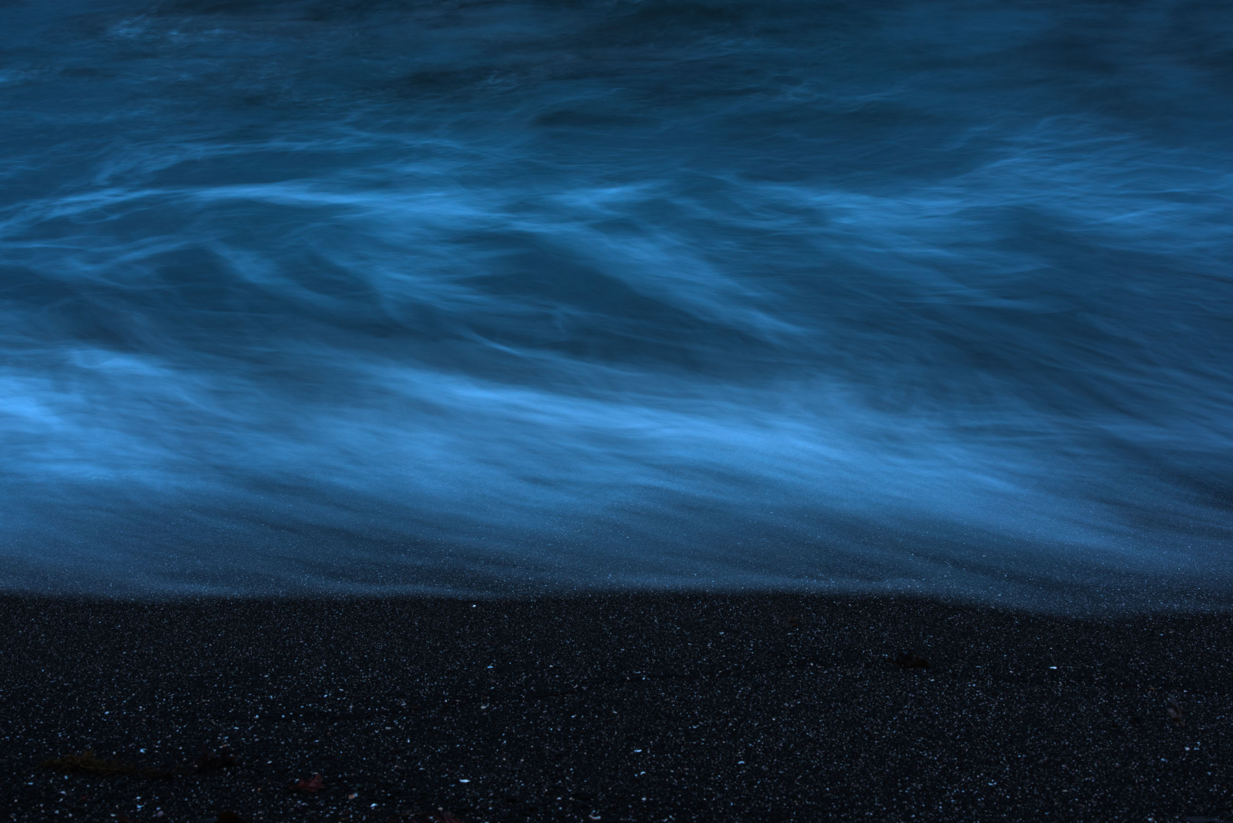 Blue water washing onto black sand