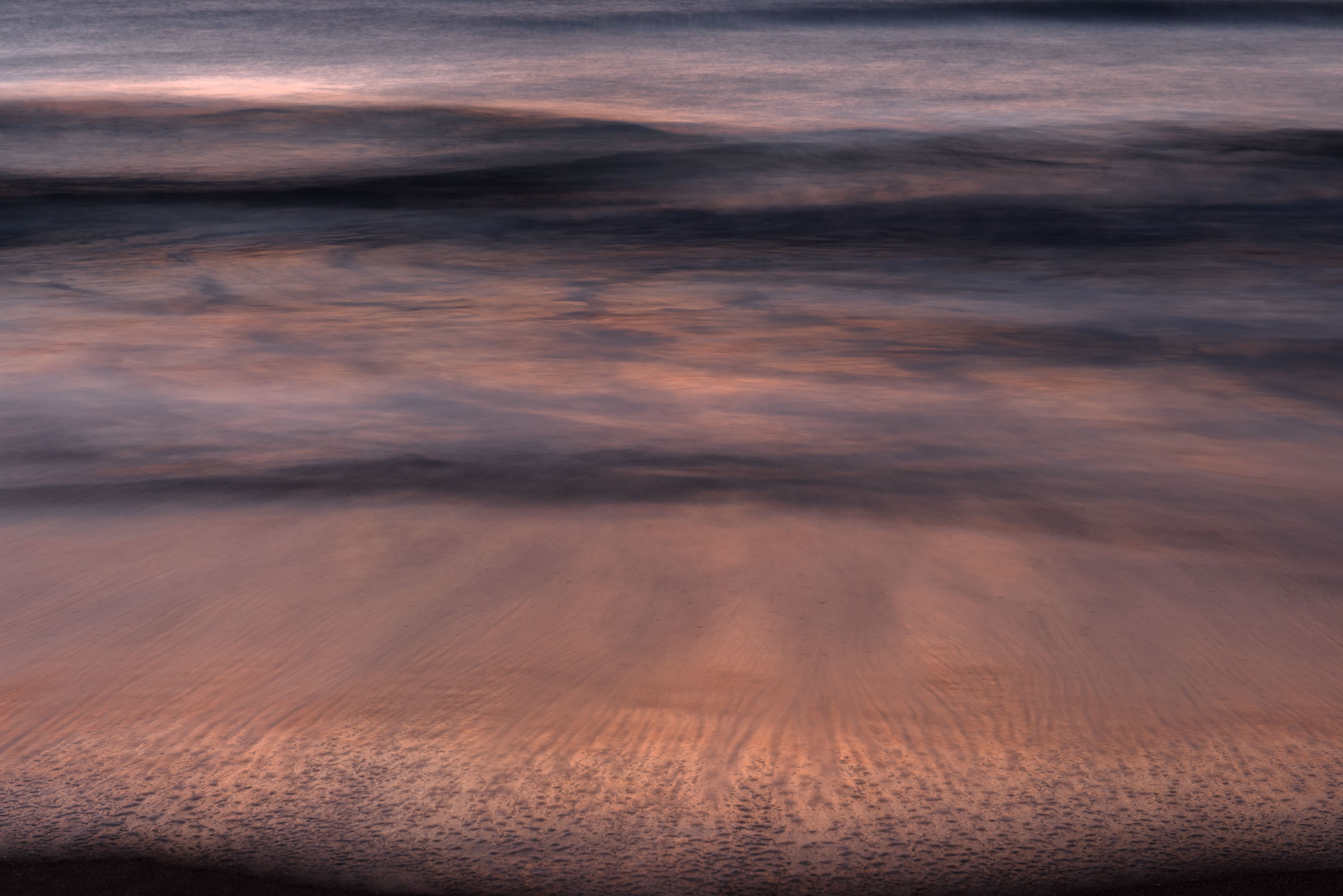 Pink evening light reflected across incoming waves
