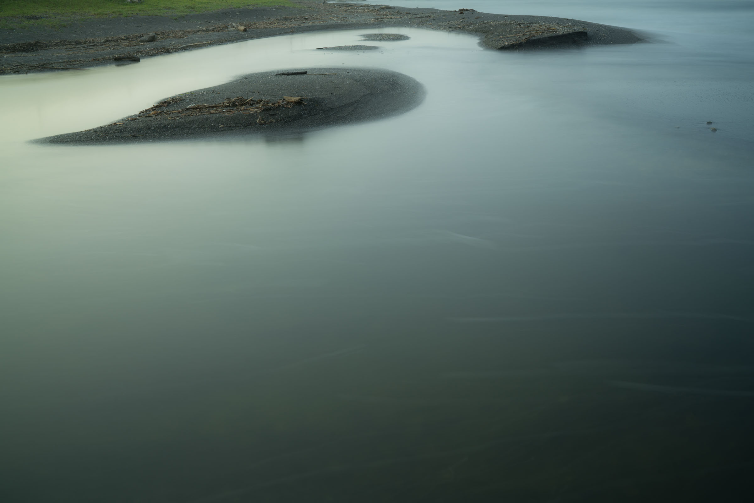 Pale water surrounding dark sandbars and driftwood
