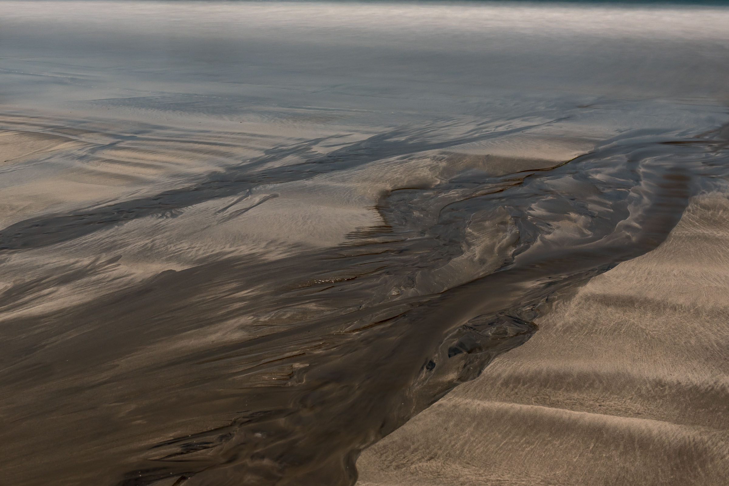 Water channels spreading across layered wet sand