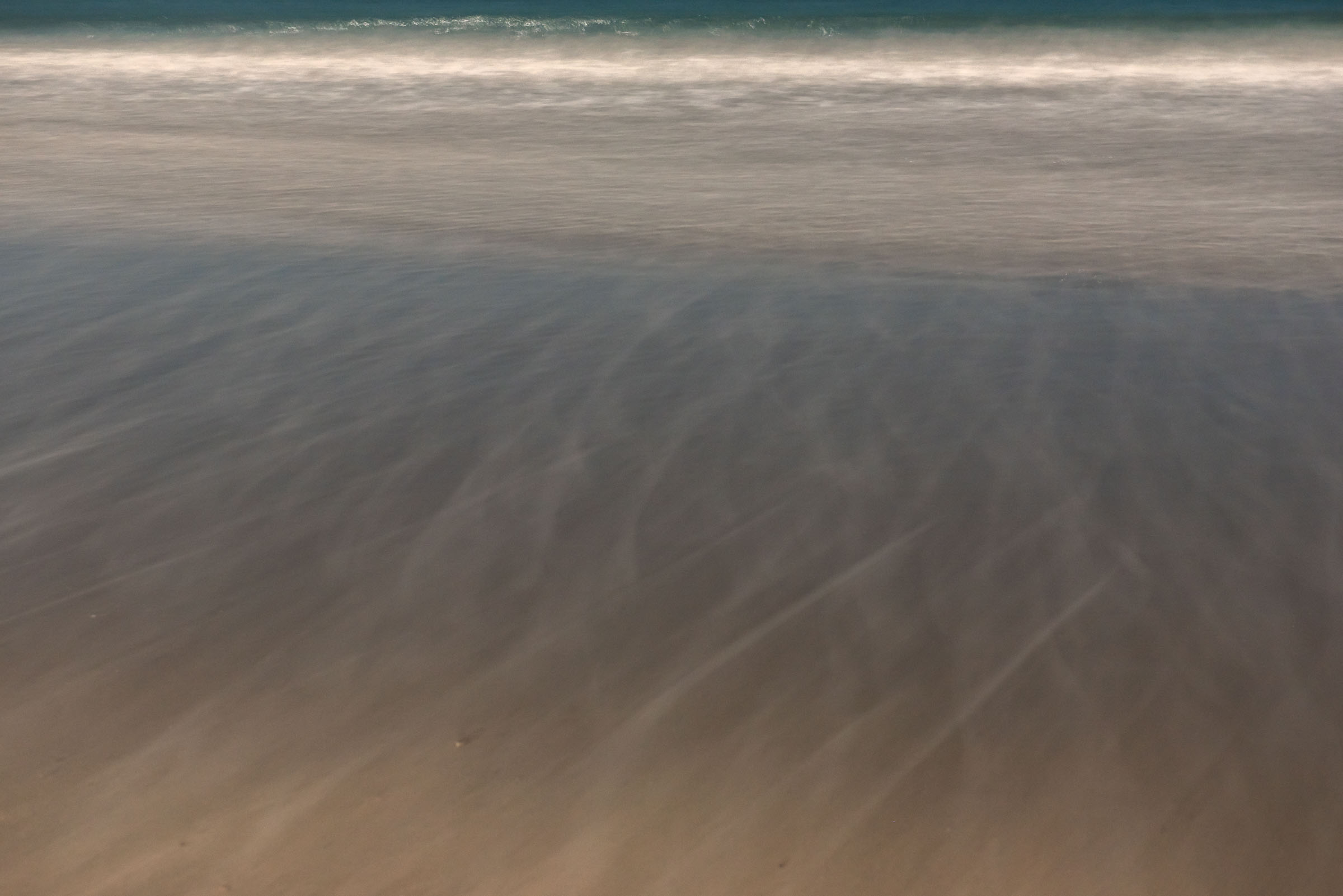 A thin wave breaking over smooth wet sand