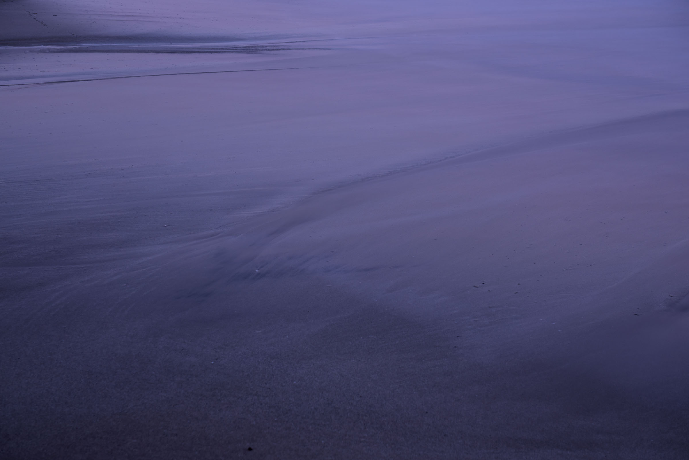 Purple-blue tide patterns across wet beach sand