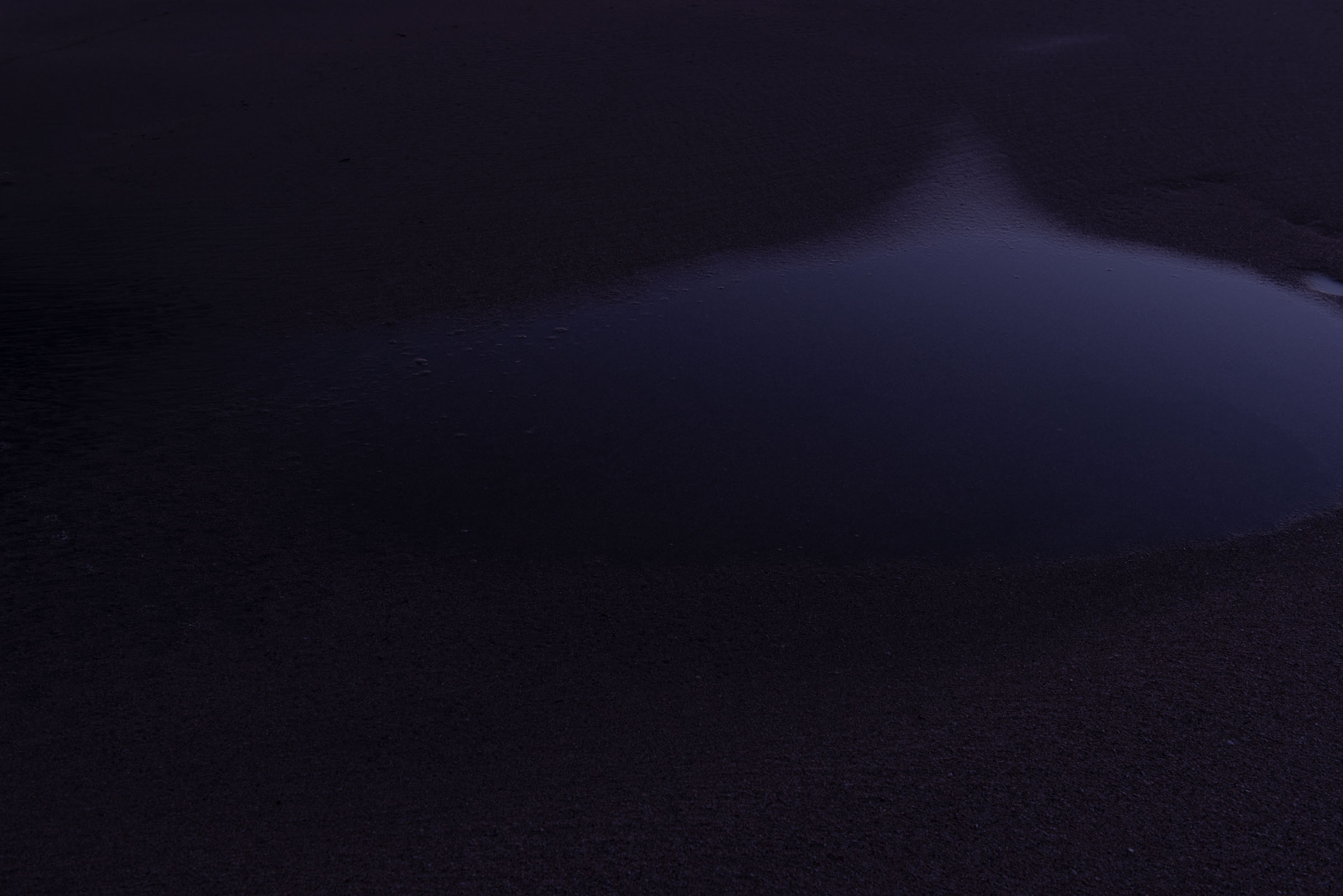 A dark pool edged by black sand