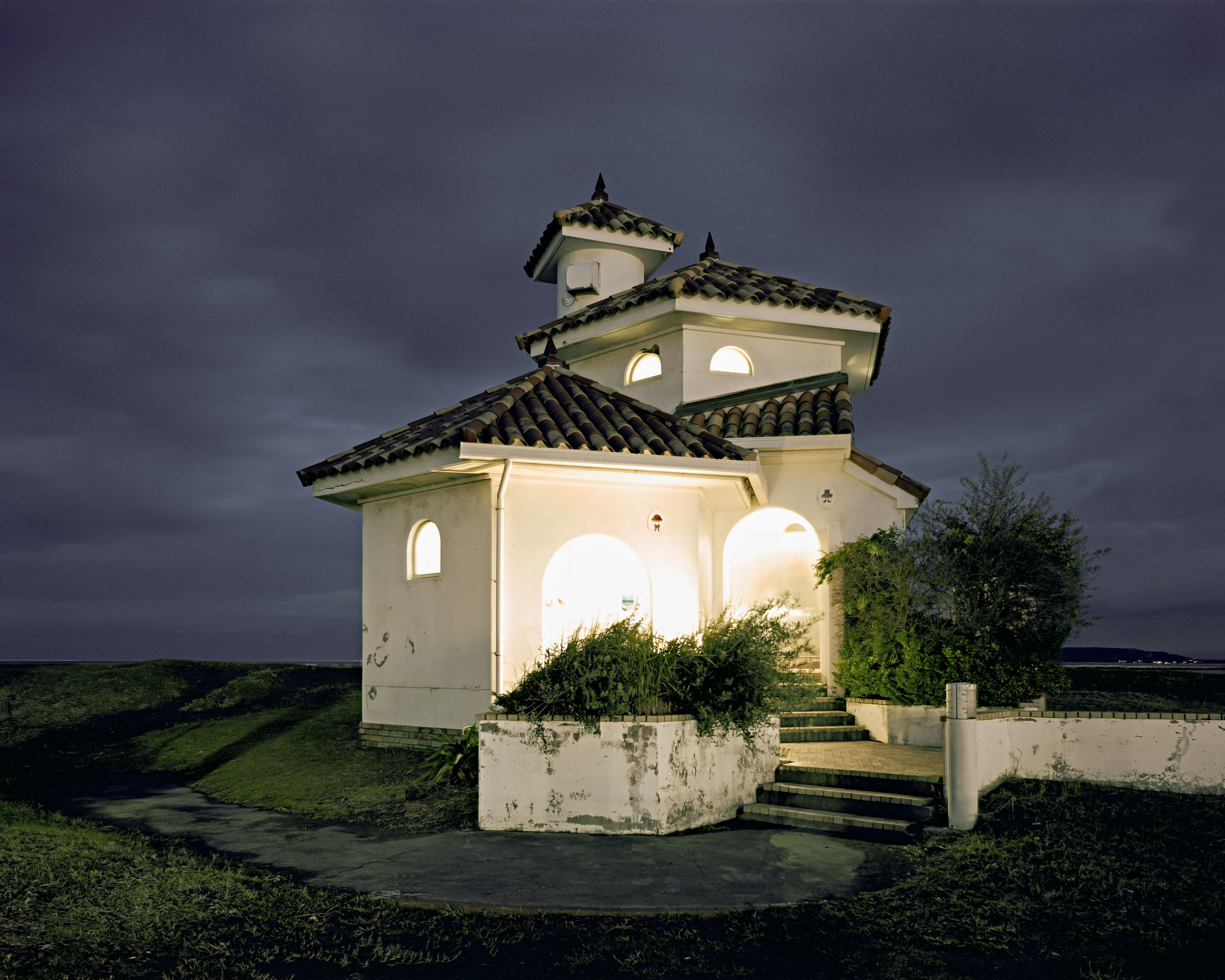 White public toilet with tiled roofs, glowing arched entrances and shrubs