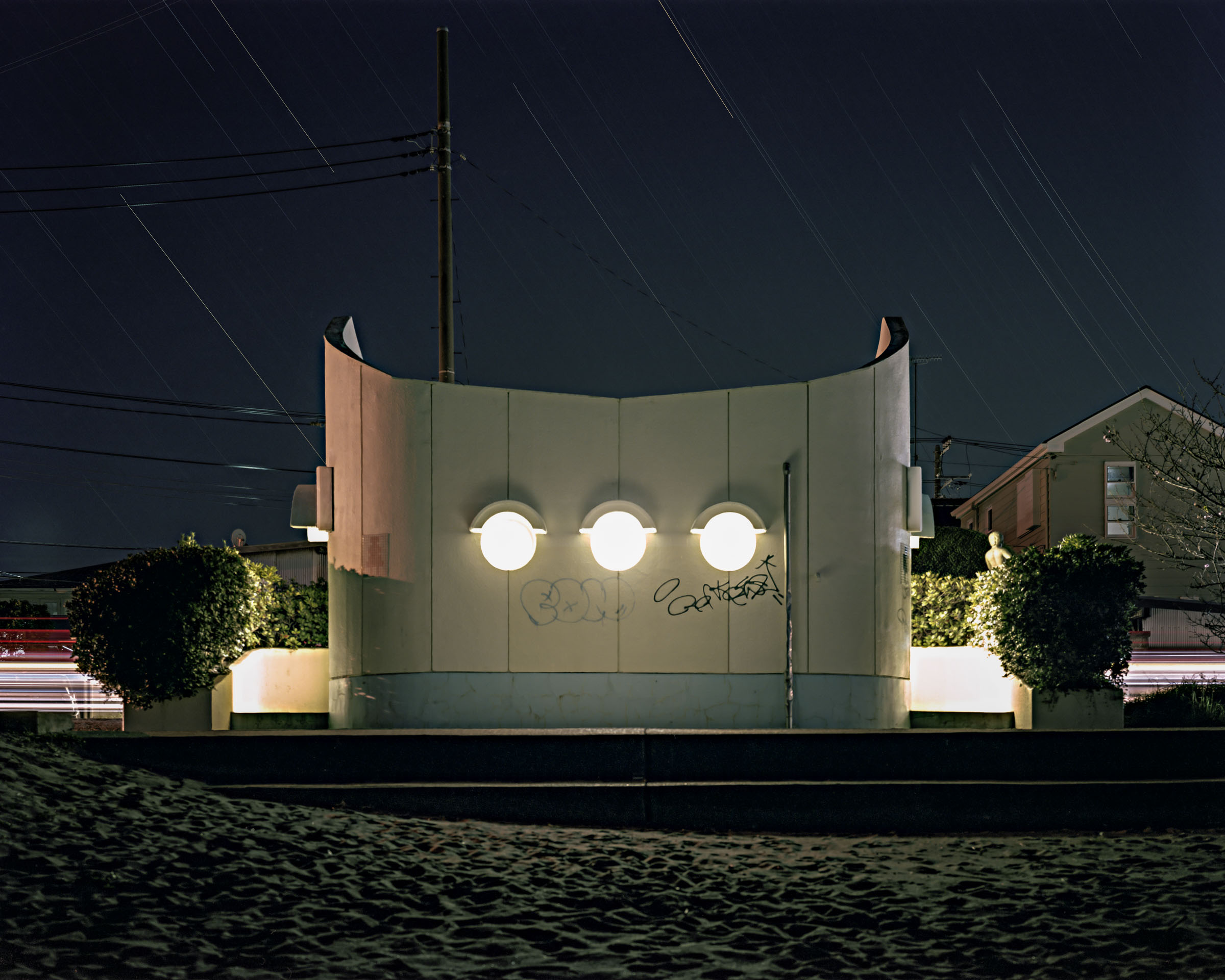 Curved public toilet wall with three round lights, graffiti and star trails