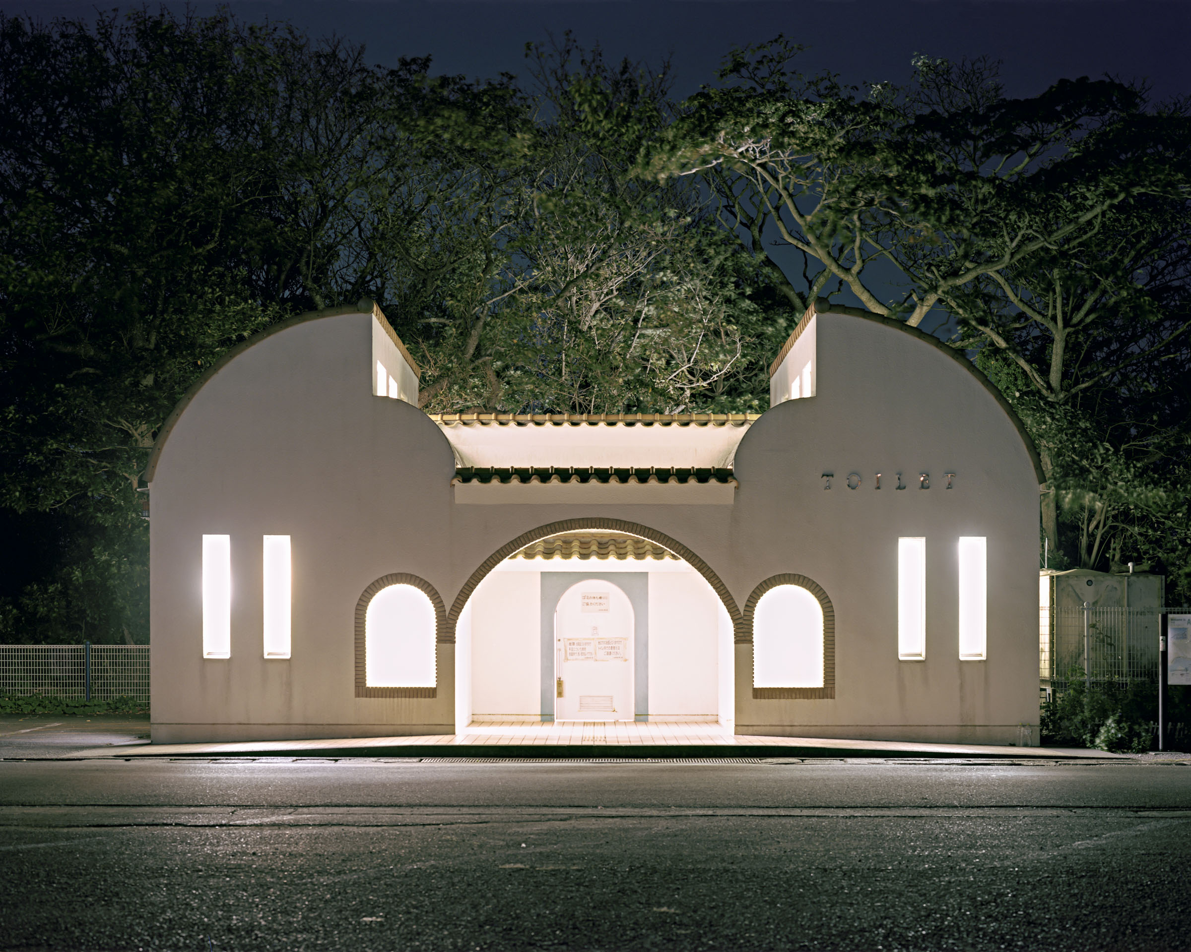 Symmetrical white public toilet with an arched entrance backed by trees