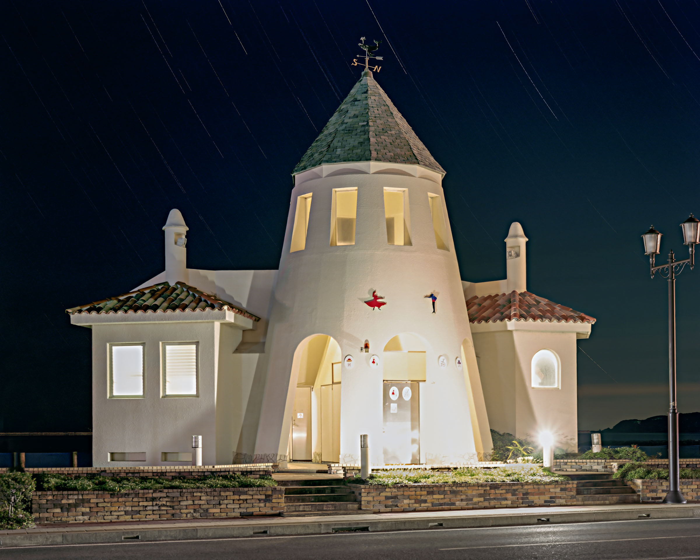 White public toilet building illuminated at night beneath star trails