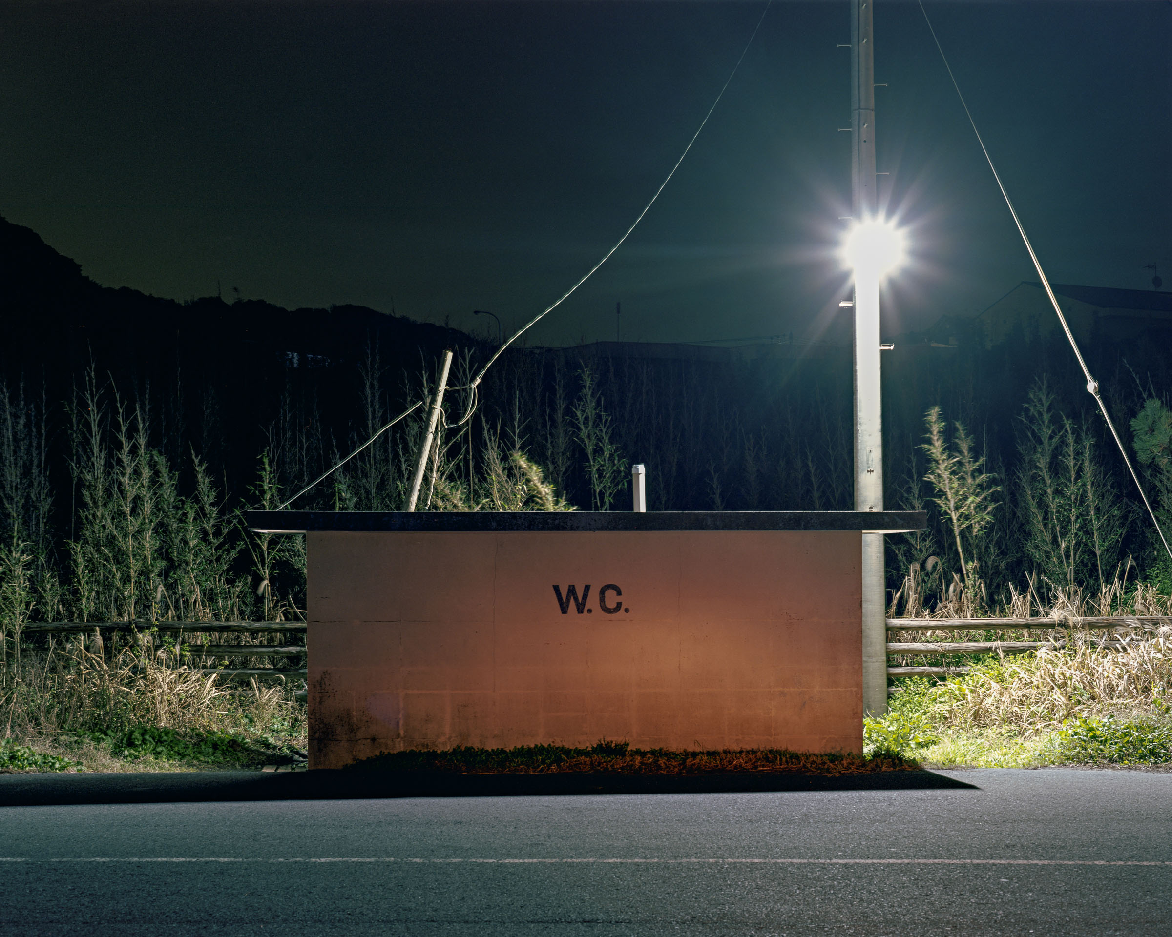 Low public toilet marked W.C. beneath a bright streetlight