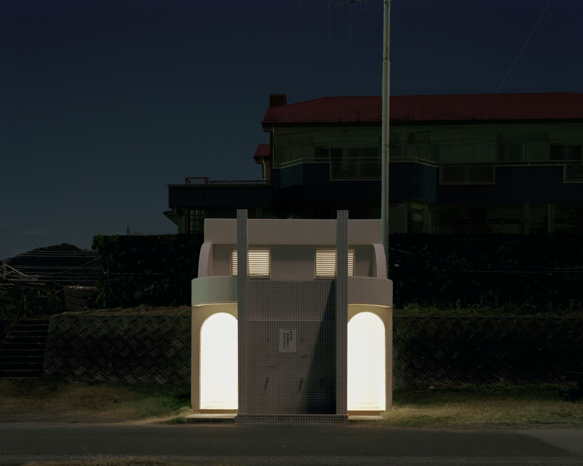 Narrow white public toilet with illuminated arched doorways below a larger building