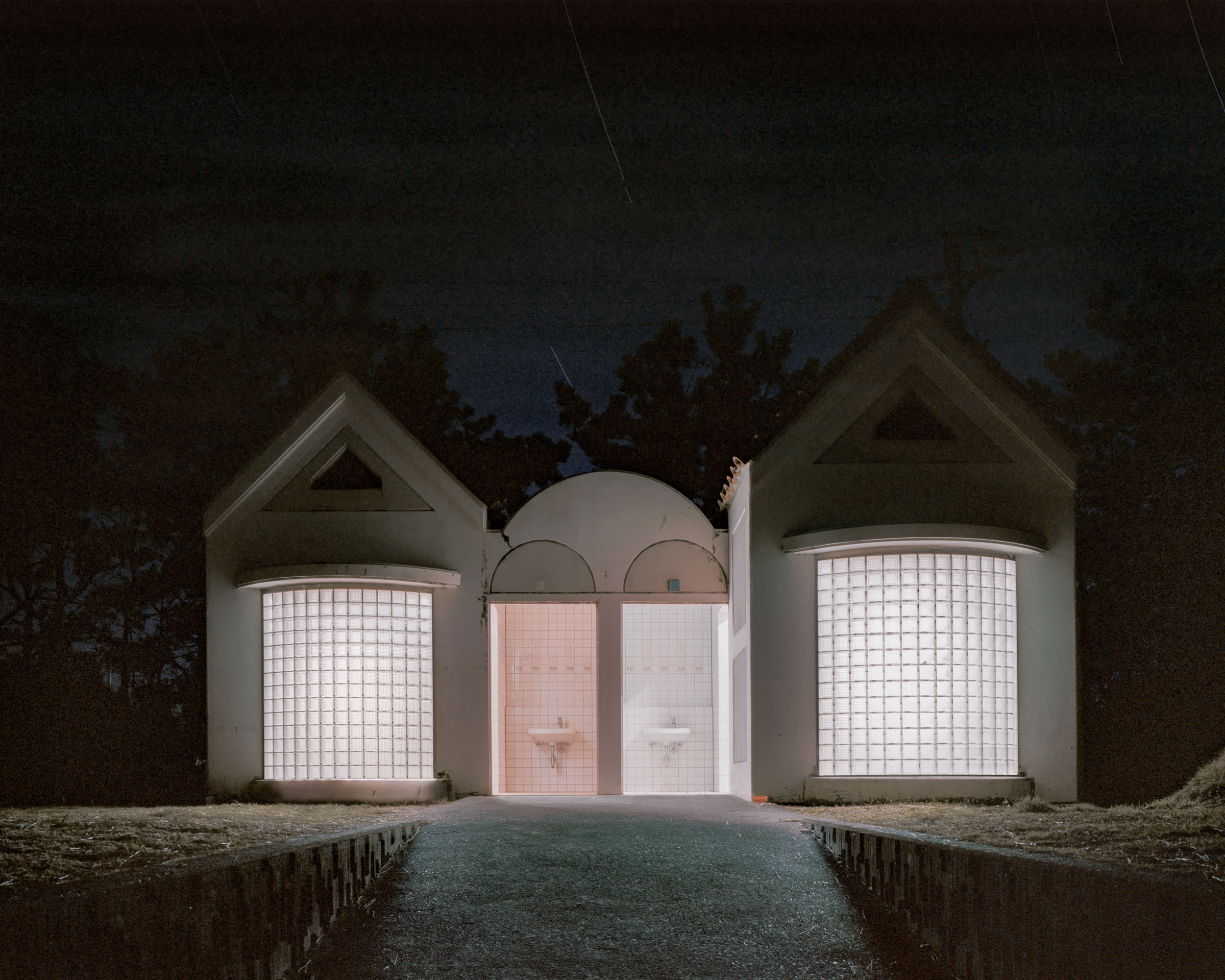 Symmetrical public toilet with two glass-block bays and open central washbasins