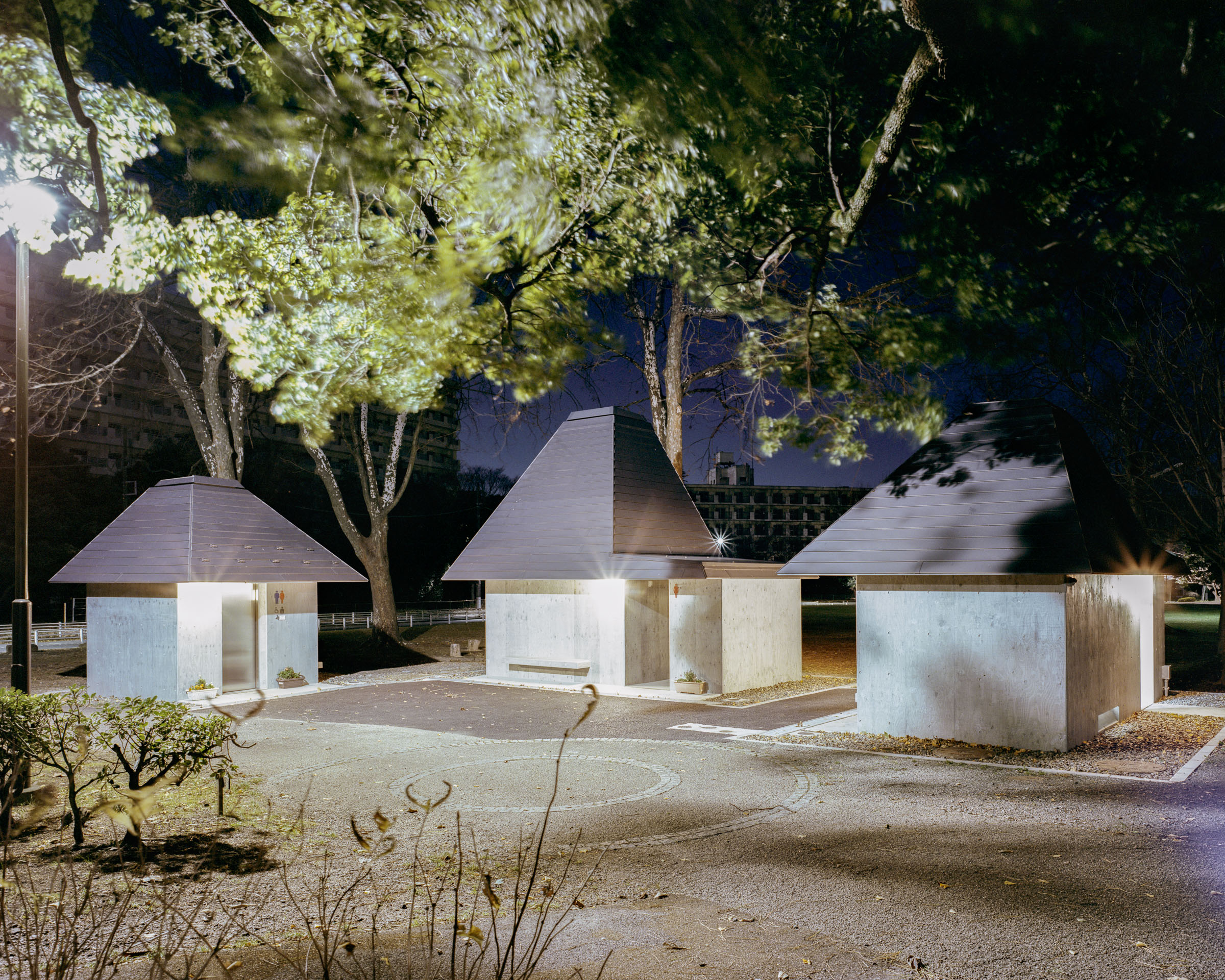 Three small pyramid-roofed toilet structures under trees