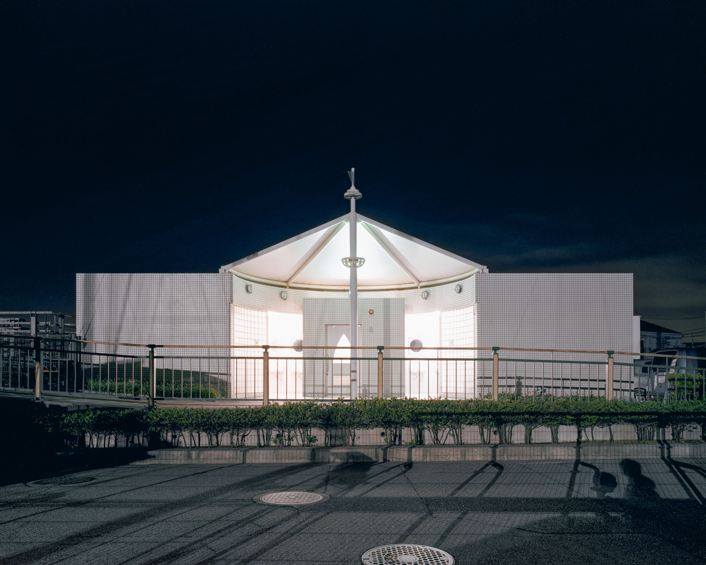 Tiled public toilet with a bright tent-like central roof behind a railing