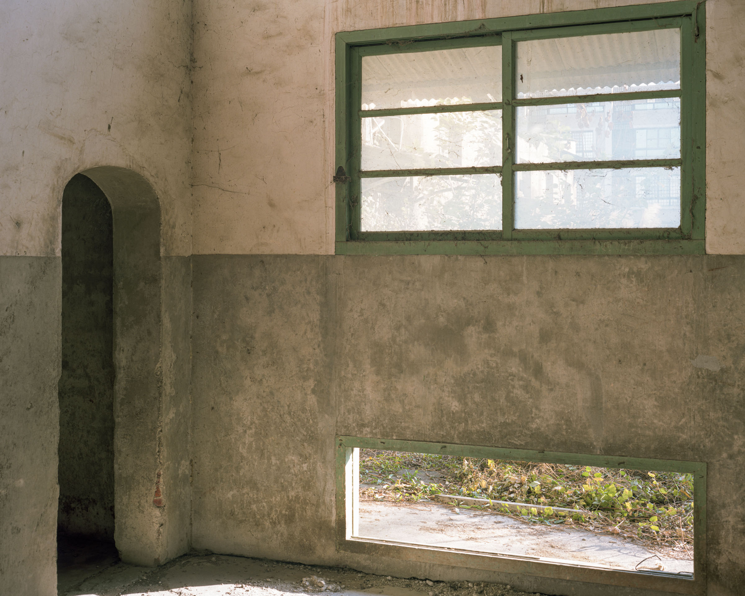 Abandoned interior with a green-framed window and arched doorway