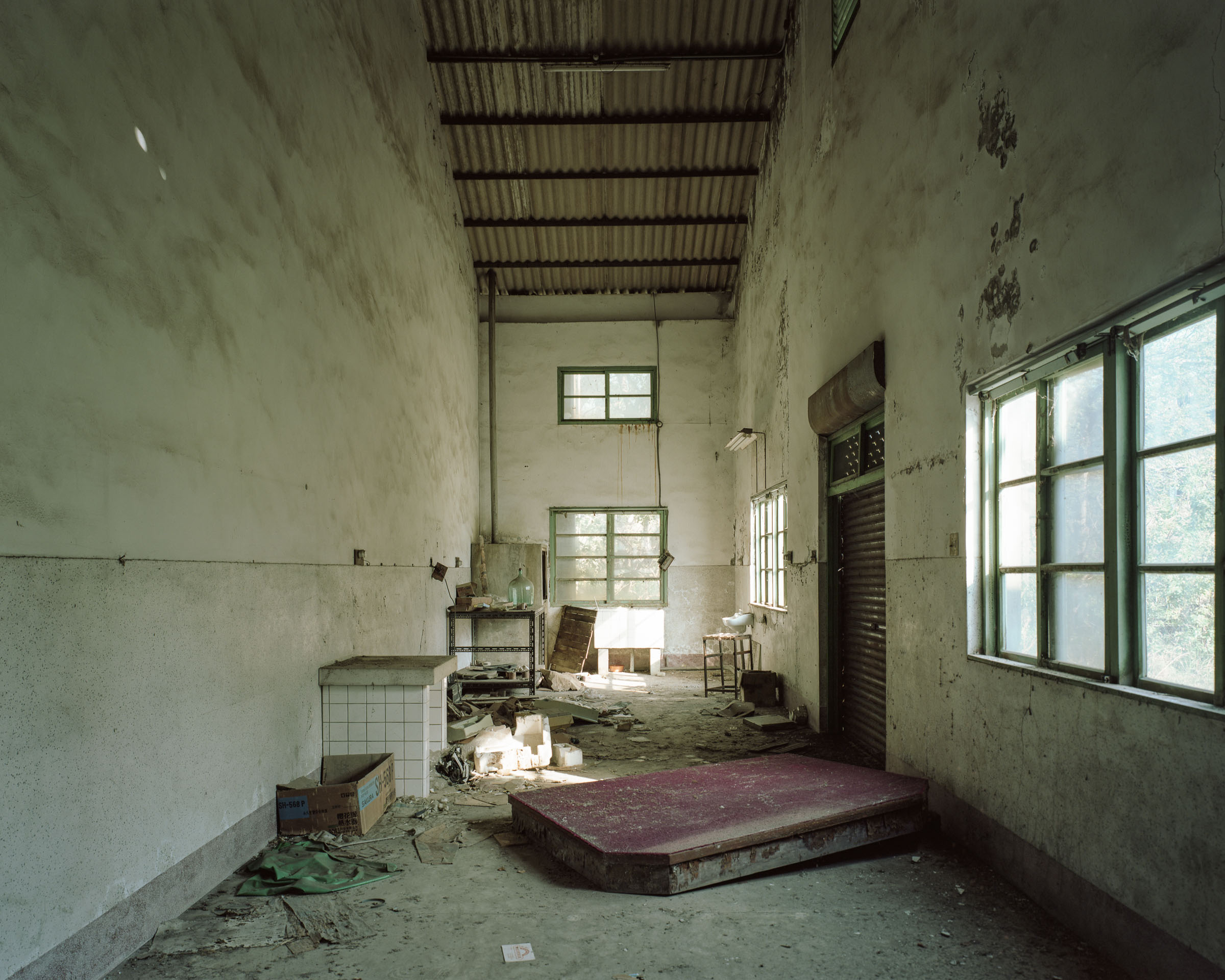 Abandoned industrial room with debris and a large platform under a tall ceiling
