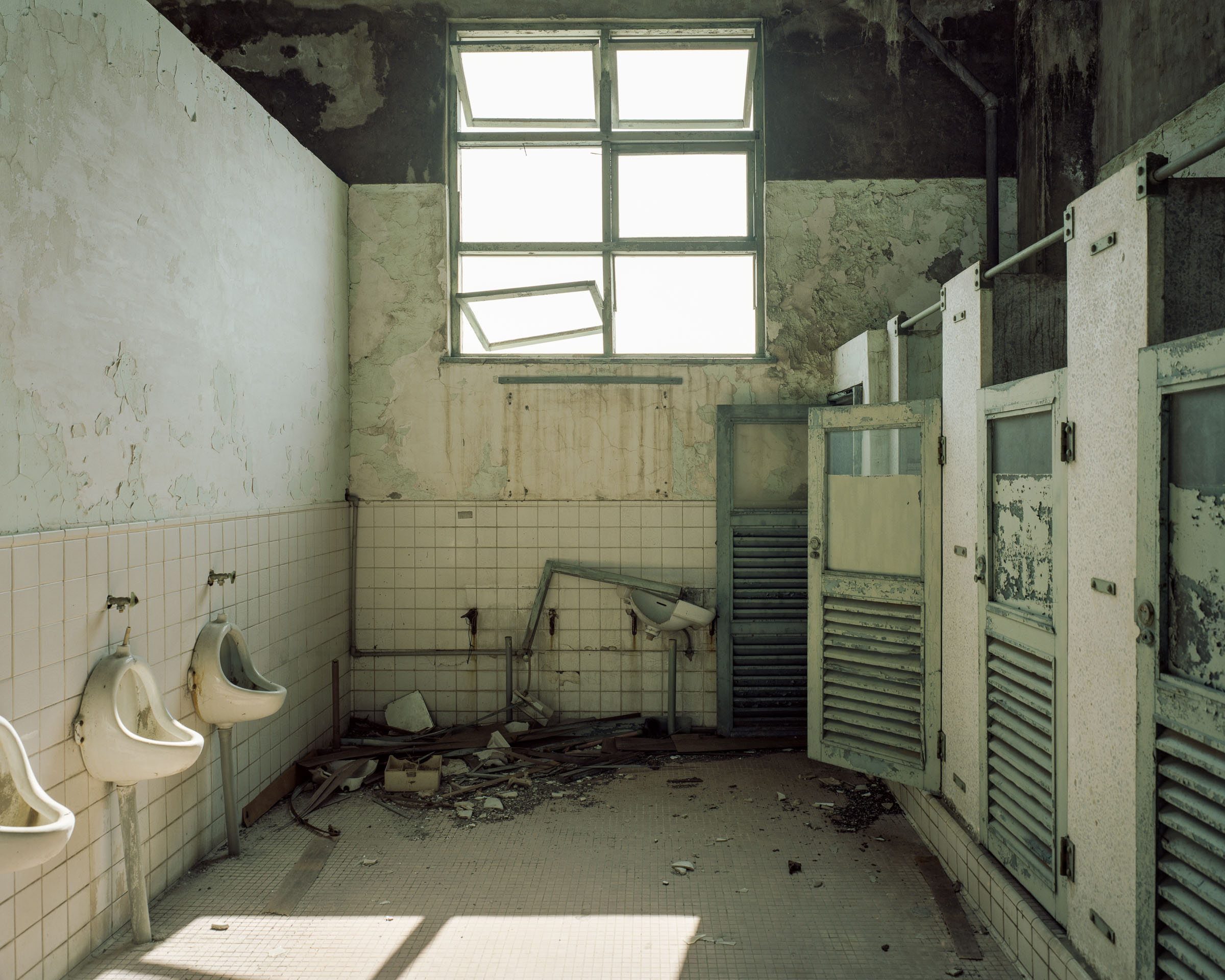 Derelict washroom with urinals, open stall doors and debris