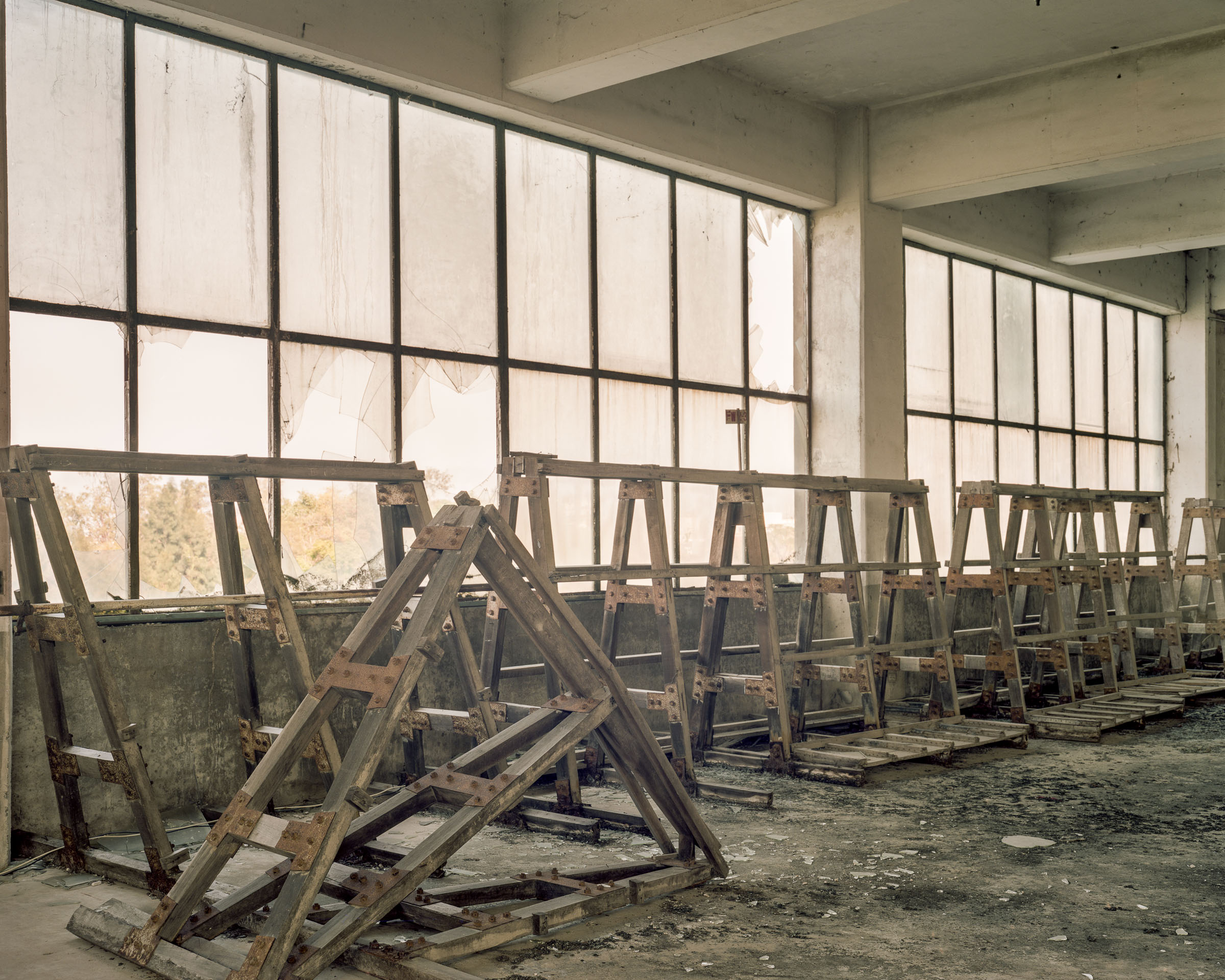 Rows of wooden support frames below broken factory windows