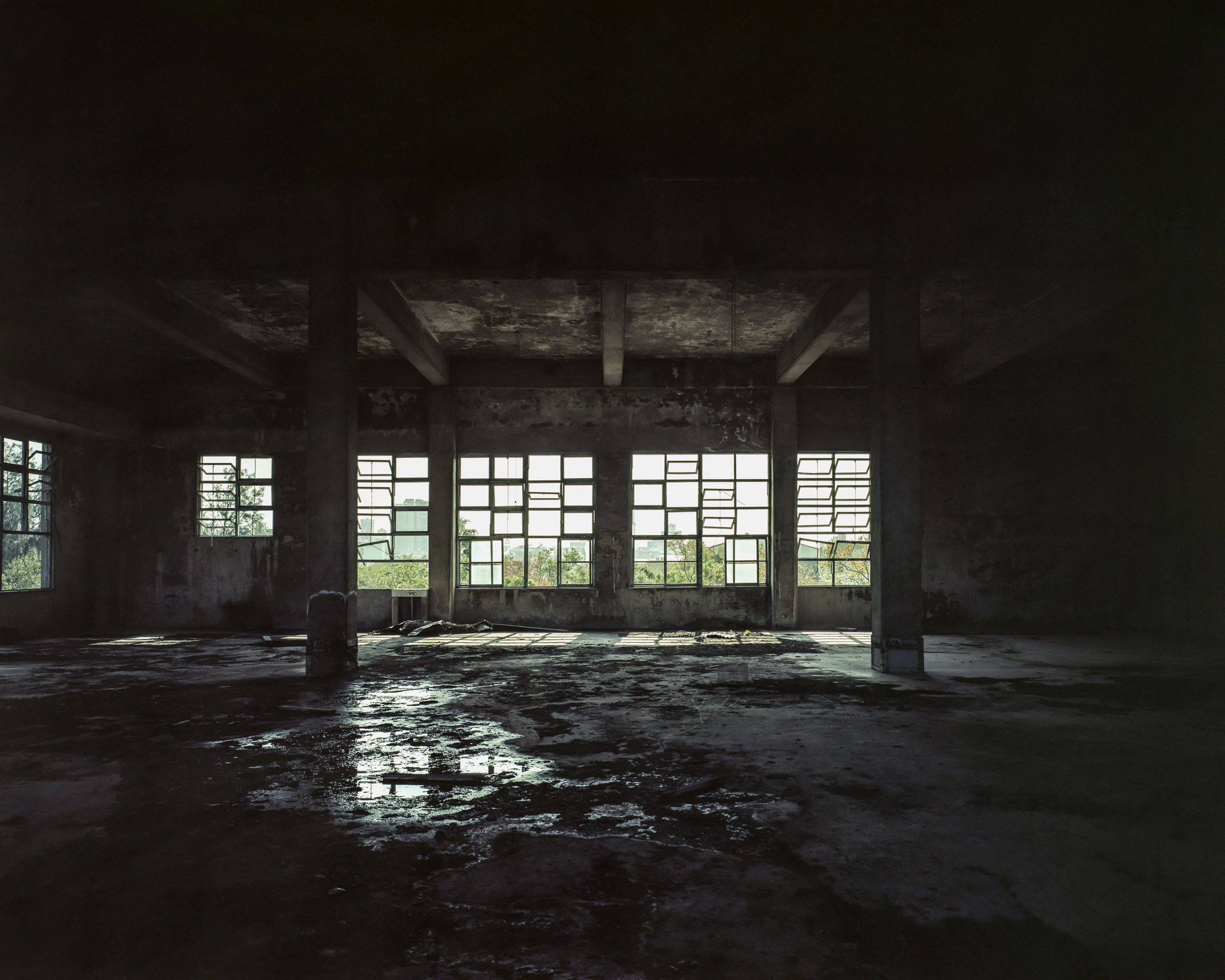 Sunlit windows reflected on a dark factory floor